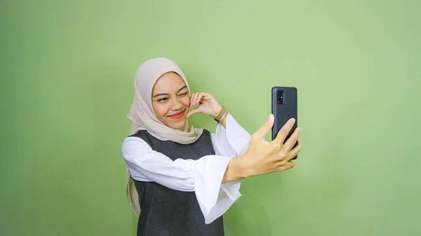 陽気な若いアジアの女性が自撮り 緑の背景に隔離されたスマートフォンのフロントカメラを見て — ストック写真