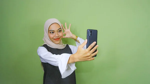 快乐的年轻亚洲女人自拍 在绿色背景下看着智能手机前置摄像头 — 图库照片