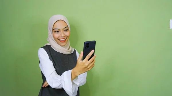 幸せな笑顔若いアジアの女性でカジュアルシャツ 緑の背景に隔離されたスマートフォンでビデオ通話を持っています — ストック写真