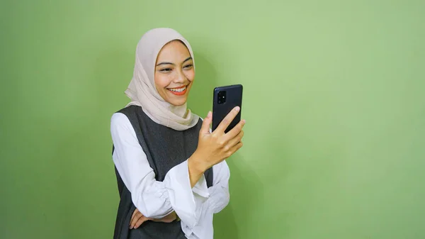 幸せな笑顔若いアジアの女性でカジュアルシャツ 緑の背景に隔離されたスマートフォンでビデオ通話を持っています — ストック写真