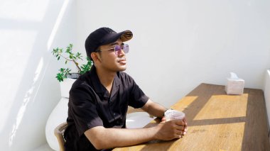 Yogyakarta - 4 Temmuz 2023 - Siyah gömlekli ve şapkalı yakışıklı Asyalı kahve içiyor 