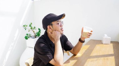 Yogyakarta - 4 Temmuz 2023 - Siyah gömlekli ve şapkalı yakışıklı Asyalı kahve içiyor 