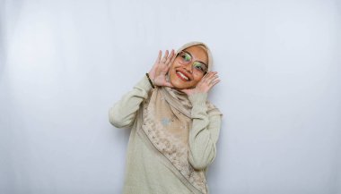 Genç ve güzel Asyalı Müslüman bir kadın başörtüsü takıyor ve eli ağzında bağırıyor ve bağırıyor. iletişim konsepti.