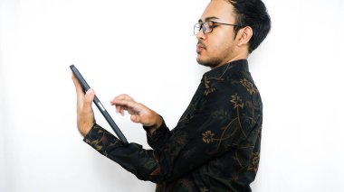Batik giyen Asyalı genç bir adamın portresi beyaz arka planda tablet bilgisayar kullanıyor.