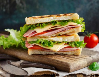 İçinde jambon, peynir ve marul bulunan bir panini koleksiyonu, düzgünce bir kesim tahtasına yerleştirilmiş.