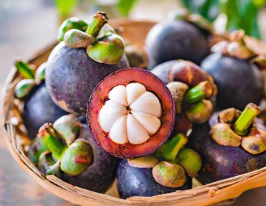 Eski ahşap bir arka planda bambu sepetinde sunulan taze mangosen yavruları. Mangosteen, meyvelerin kraliçesi olarak tanınır ve Asya meyvelerinin özünü yakalar..