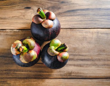 Eski ahşap bir arka planda bambu sepetinde sunulan taze mangosen yavruları. Mangosteen, meyvelerin kraliçesi olarak tanınır ve Asya meyvelerinin özünü yakalar..