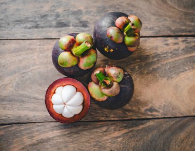 Eski ahşap bir arka planda bambu sepetinde sunulan taze mangosen yavruları. Mangosteen, meyvelerin kraliçesi olarak tanınır ve Asya meyvelerinin özünü yakalar..