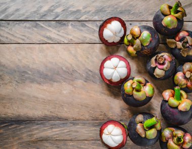 Eski ahşap bir arka planda bambu sepetinde sunulan taze mangosen yavruları. Mangosteen, meyvelerin kraliçesi olarak tanınır ve Asya meyvelerinin özünü yakalar..