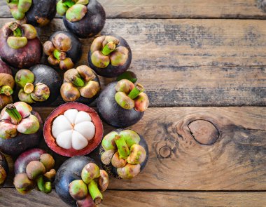 Eski ahşap bir arka planda bambu sepetinde sunulan taze mangosen yavruları. Mangosteen, meyvelerin kraliçesi olarak tanınır ve Asya meyvelerinin özünü yakalar..