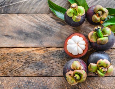 Eski ahşap bir arka planda bambu sepetinde sunulan taze mangosen yavruları. Mangosteen, meyvelerin kraliçesi olarak tanınır ve Asya meyvelerinin özünü yakalar..