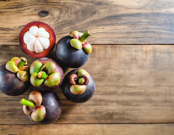 Eski ahşap bir arka planda bambu sepetinde sunulan taze mangosen yavruları. Mangosteen, meyvelerin kraliçesi olarak tanınır ve Asya meyvelerinin özünü yakalar..