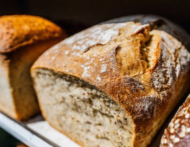 İyi aydınlatılmış bir fırının ahşap raflarında sergilenen taze ekmek çeşitleri, altın kabuklu çeşitli somunların yer aldığı.