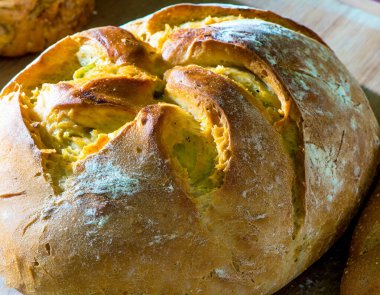 İyi aydınlatılmış bir fırının ahşap raflarında sergilenen taze ekmek çeşitleri, altın kabuklu çeşitli somunların yer aldığı.