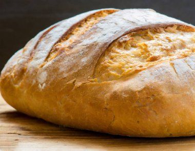 İyi aydınlatılmış bir fırının ahşap raflarında sergilenen taze ekmek çeşitleri, altın kabuklu çeşitli somunların yer aldığı.