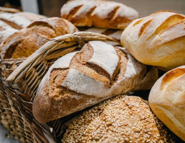 İyi aydınlatılmış bir fırının ahşap raflarında sergilenen taze ekmek çeşitleri, altın kabuklu çeşitli somunların yer aldığı.