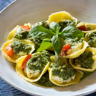 Tahta masa, içinde ricotta peyniri, fesleğen sosu ve sebze bulunan tortelloni sergiliyor..