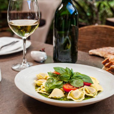 Tahta masa, içinde ricotta peyniri, fesleğen sosu ve sebze bulunan tortelloni sergiliyor..