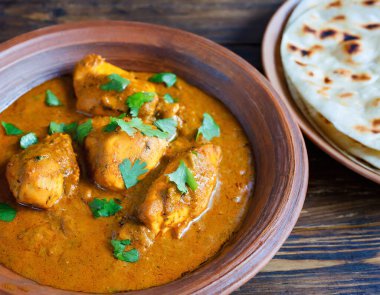 Baharatlı tavuk tikka masala kil tabakta servis edilir pirinç ve ahşap zemin üzerinde naan ekmeği.