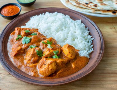 Baharatlı tavuk tikka masala kil tabakta servis edilir pirinç ve ahşap zemin üzerinde naan ekmeği.