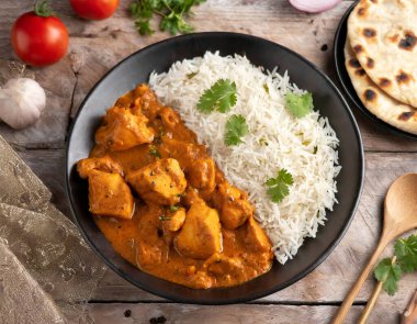 Baharatlı tavuk tikka masala kil tabakta servis edilir pirinç ve ahşap zemin üzerinde naan ekmeği.