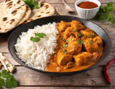 Baharatlı tavuk tikka masala kil tabakta servis edilir pirinç ve ahşap zemin üzerinde naan ekmeği.