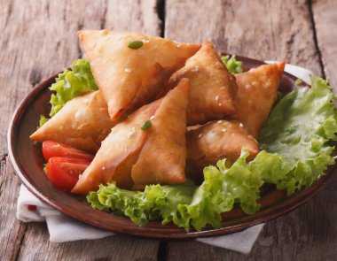Lezzetli Hint samosa pastası bir tabakta domates ve ahşap bir masada marul ile sunuluyor..