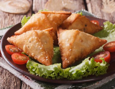 Lezzetli Hint samosa pastası bir tabakta domates ve ahşap bir masada marul ile sunuluyor..