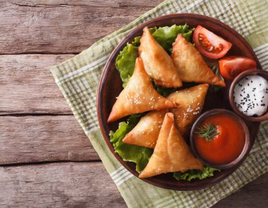 Lezzetli Hint samosa pastası bir tabakta domates ve ahşap bir masada marul ile sunuluyor..