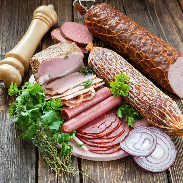 Selection of cold meats, including a variety of processed cold meat products, displayed on a wooden background.