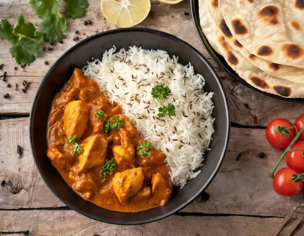 Spicy chicken tikka masala curry served in a clay plate with rice and naan bread on a wooden background.