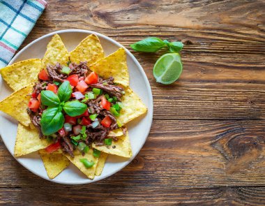 Yakın plan nachos, üzerinde sığır eti ve taze sebzeler bulunan bir Meksika yemeği, ahşap bir arka planda..