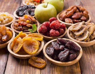 Elma, kuru erik, hurma, kayısı, kuru üzüm ve kivi gibi çeşitli kurutulmuş meyvelerle süslenmiş ahşap bir masa..