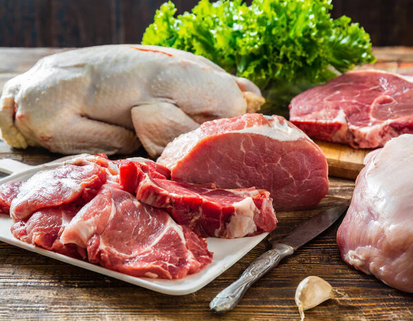 Assorted fresh meats, including pork, beef, turkey, and chicken, displayed on a wooden table.