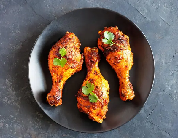 Top view, flat lay of Indian-style tandoori chicken presented on a plate over a dark stone background. The chicken legs are marinated in yogurt and spices.