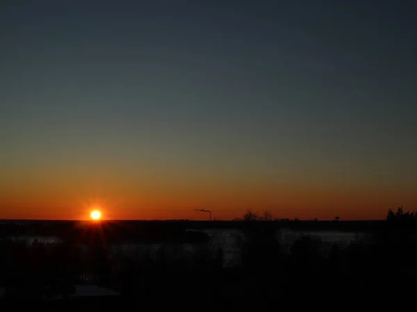 Sunset in Helsinki. An orange and  a turquoise sky. The yellow sun with red rays. Sunset in a winter evening. The sun above the horizon. A chimney in a background.