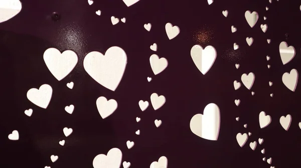 White hearts engraved in a wall. Some small and big hearts on the wall. The wall is dark lila. Background behind the wall is white. A hearts wallpaper photo.