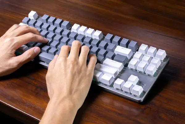 A modern mechanical keyboard and hands on a wooden table. After some edits.