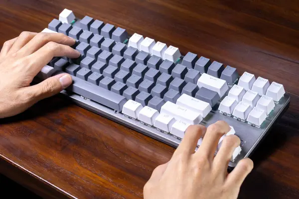 A modern mechanical keyboard and hands on a wooden table. After some edits.
