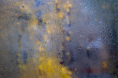 Doğal su damlalarının dokusu renkli lekelerin arka planına karşı cam üzerine düşer. Sonbaharda penceredeki buğulanma