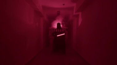 Elinde kırmızı bir kılıçla Darth Vader koridorda fırtına birlikleriyle yürüyor.