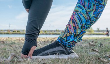 Genç şişman kadın gölün yanındaki parkta bacaklarını esnetiyor. Hea!