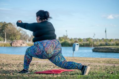 Genç şişman kadın gölün yanındaki parkta yoga yapıyor. Sağlıklı