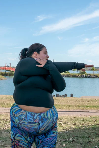 年轻的胖女人在湖边的公园里伸展着她的身体 — 图库照片