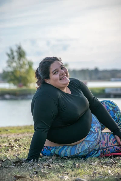 年轻的胖女人在湖边的公园里伸展着她的身体 — 图库照片