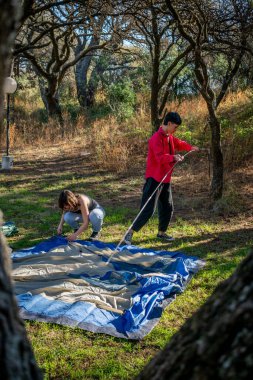 İki arkadaş kamp alanında çadır kuruyor.