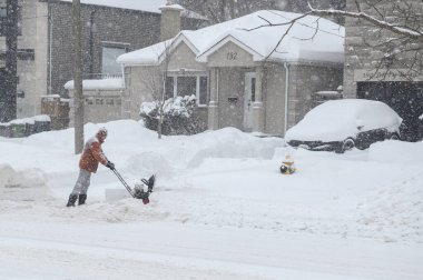 Toronto, ON, Kanada - 27 Şubat 2025: Bir adam varoş mahallesinde yoğun kar yağışı sırasında garaj yolundaki derin karı temizlemek için kar temizleme makinesi kullanıyor.