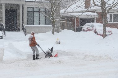 Toronto, ON, Kanada - 27 Şubat 2025: Bir adam varoş mahallesinde yoğun kar yağışı sırasında garaj yolundaki derin karı temizlemek için kar temizleme makinesi kullanıyor.