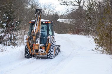 Toronto, ON, Kanada - 27 Şubat 2025: Güvenlik ekipmanlı iki işçiyle kar küreme aracı kar kaplı kırsal bir yolu temizliyor, soğuk bir kış gününde taze karı kenara itiyor.