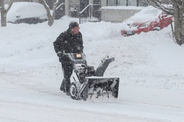 Toronto, ON, Kanada - 27 Şubat 2025: Bir adam varoş mahallesinde yoğun kar yağışı sırasında garaj yolundaki derin karı temizlemek için kar temizleme makinesi kullanıyor.